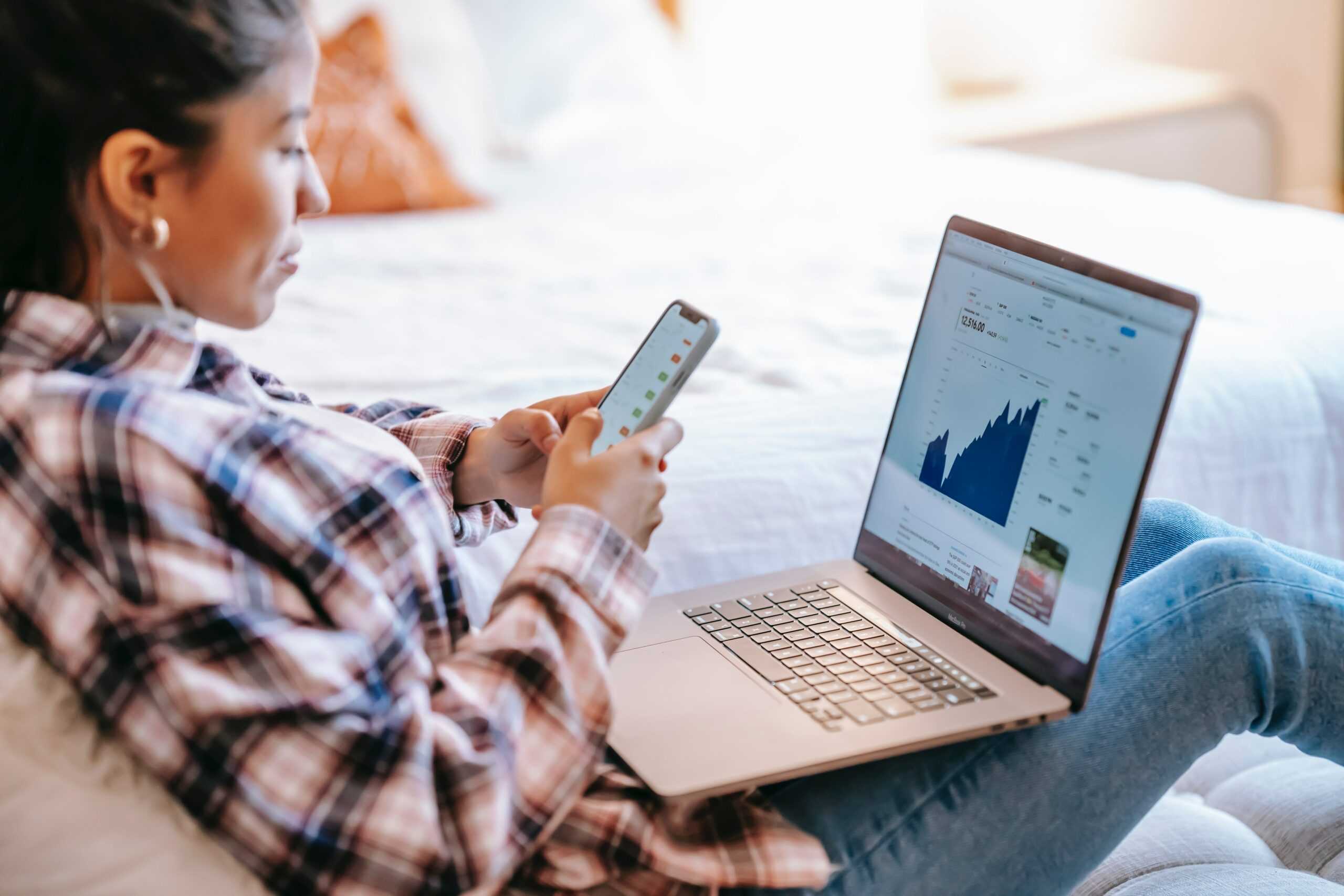 A person is seated, using their phone and laptop, analyzing social media trend data